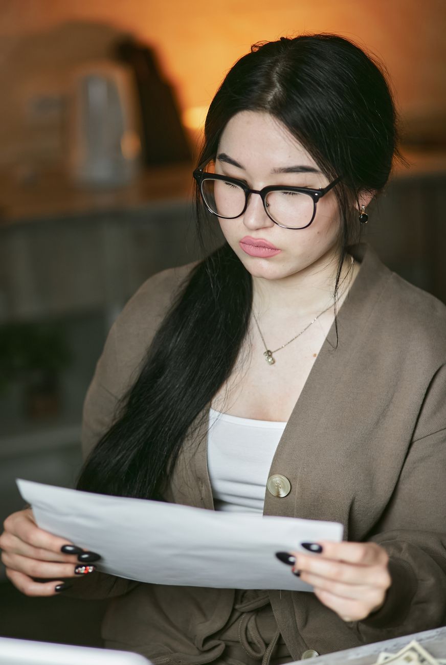 A woman in glasses reading closely through a document